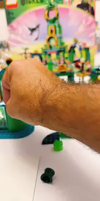 A hand reaches toward a LEGO set with a green castle in the background.