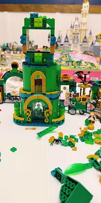 A green LEGO structure under construction with scattered pieces, featuring a castle in the background.