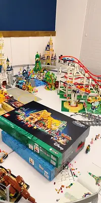 A table filled with various LEGO Disney sets, including castles, a roller coaster, and a large box for a LEGO Disney set.